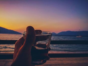 Low section of woman on beach against sky during sunset