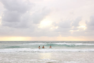 People at beach against sky during sunset