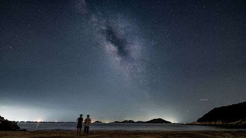 People on shore against sky at night