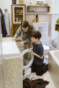 Teenage sister assisting brother while doing laundry in bathroom at home