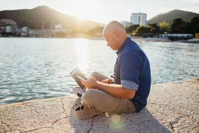 Side view of man using mobile phone while sitting on promenade