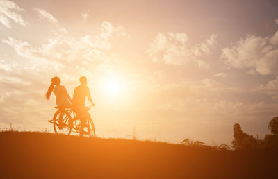 People riding bicycle against sky during sunset