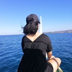 Rear view of woman sitting in boat on sea against clear blue sky