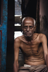 Portrait of shirtless senior man sitting at doorway