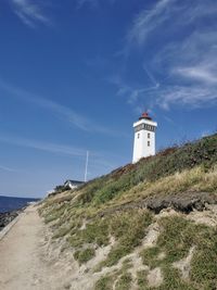 Lighthouse on beach by sea against sky