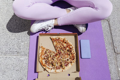 Female athlete sitting cross-legged in front of pizza on exercise mat