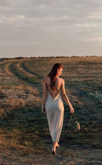 Girl with long hair walks  outdoors. beautiful teenage girl model in a dress walk across the field.