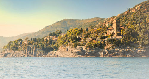 Rippled river water with houses and trees on cliff against clear sky