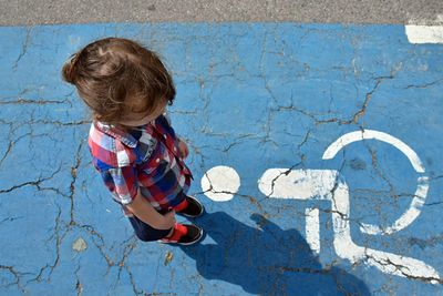 High angle view of boy standing on disabled sign