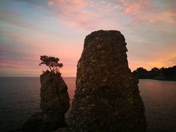 Rock formation in sea against sky during sunset