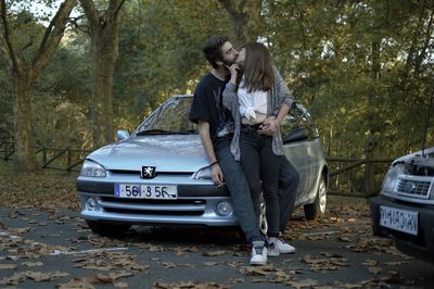 Side view of couple standing by car on trees