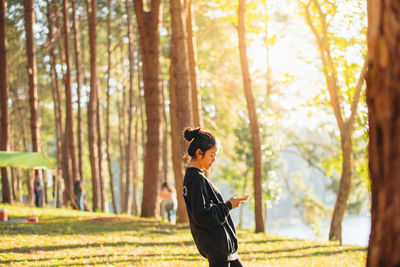 Side view of woman using mobile phone while standing in forest