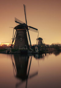 Traditional windmill by river against sky during sunset