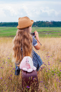 Child girl with long hair in straw hat dress on vintage suitcase taking a picture cute kid soft toy