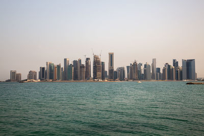 Sea by modern buildings against clear sky