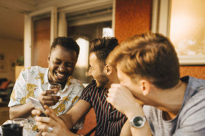 Cheerful male friends using smart phone while having fun in dinner party