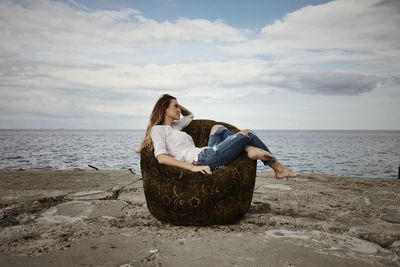 Woman sitting on sand at beach against sky