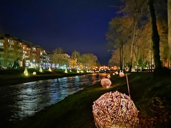 Illuminated city by lake against sky at night