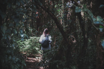 Rear view of woman with backpack standing by plants in forest