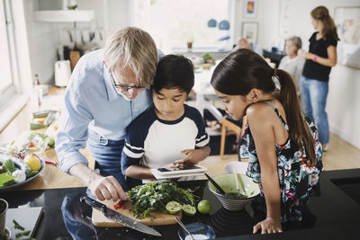 Grandfather and children preparing food in kitchen