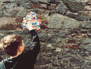 Rear view of boy with arms raised against wall