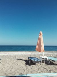 Deck chairs on beach against clear blue sky