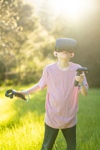 Teen using vr goggles and controllers outside in sunny field