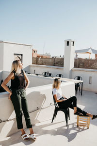 Friends relaxing on building terrace against clear sky