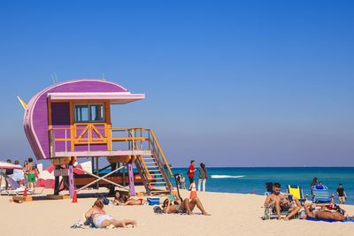 People at beach against clear blue sky