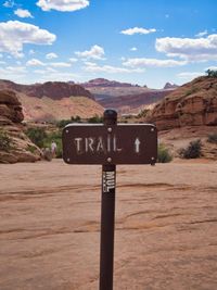 Sign board on mountain road against sky