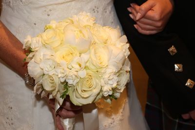 Midsection of bride holding bouquet by groom