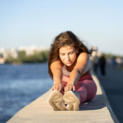 Full length of woman exercising on wall by river