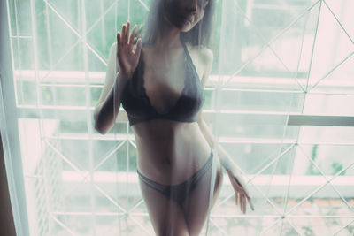 Sensuous young woman in lingerie seen through curtain at home