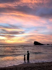 Silhouette people on beach against sky during sunset