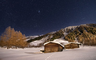 Scenic view of snowcapped landscape with wooden cottages against sky at night