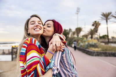 Happy woman kissing friend on cheek at promenade