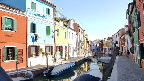 Boats moored in canal amidst buildings against sky in city