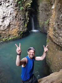 High angle portrait of man gesturing while standing on rock against river