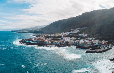 Scenic view of a town by the sea and mountains against sky