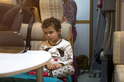 In a motorhome, a child waits for his mother to cook dinner for him, sitting on a tablet. 