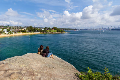 Rear view of people sitting on rock looking at sea