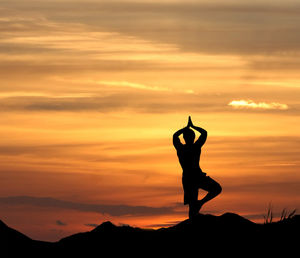 Silhouette man with arms outstretched against sky during sunset