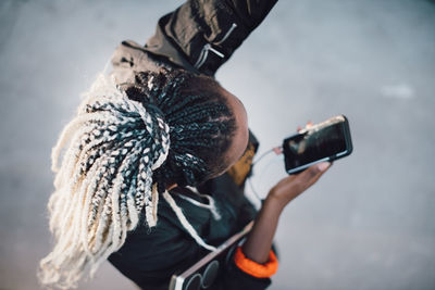 High angle view of teenage girl with dreadlocks dancing while holding smart phone at skateboard park