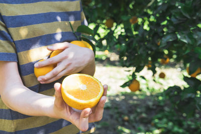 The boy is holding a half of a juicy orange in his hands.