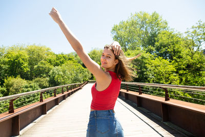Portrait of smiling teenage girl standing on footbridge against clear sky