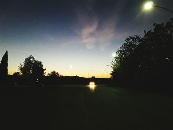 Silhouette trees by road against sky during sunset