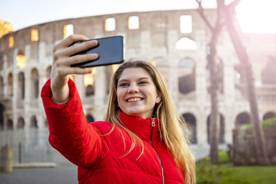 Young charming woman making a selfie in front of the colosseum during a winter vacation. 