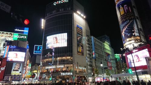 People on illuminated street amidst buildings in city at night