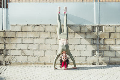 Smiling woman with hair highlights doing handstand against brick wall