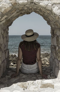 Rear view of woman sitting below arch against sea